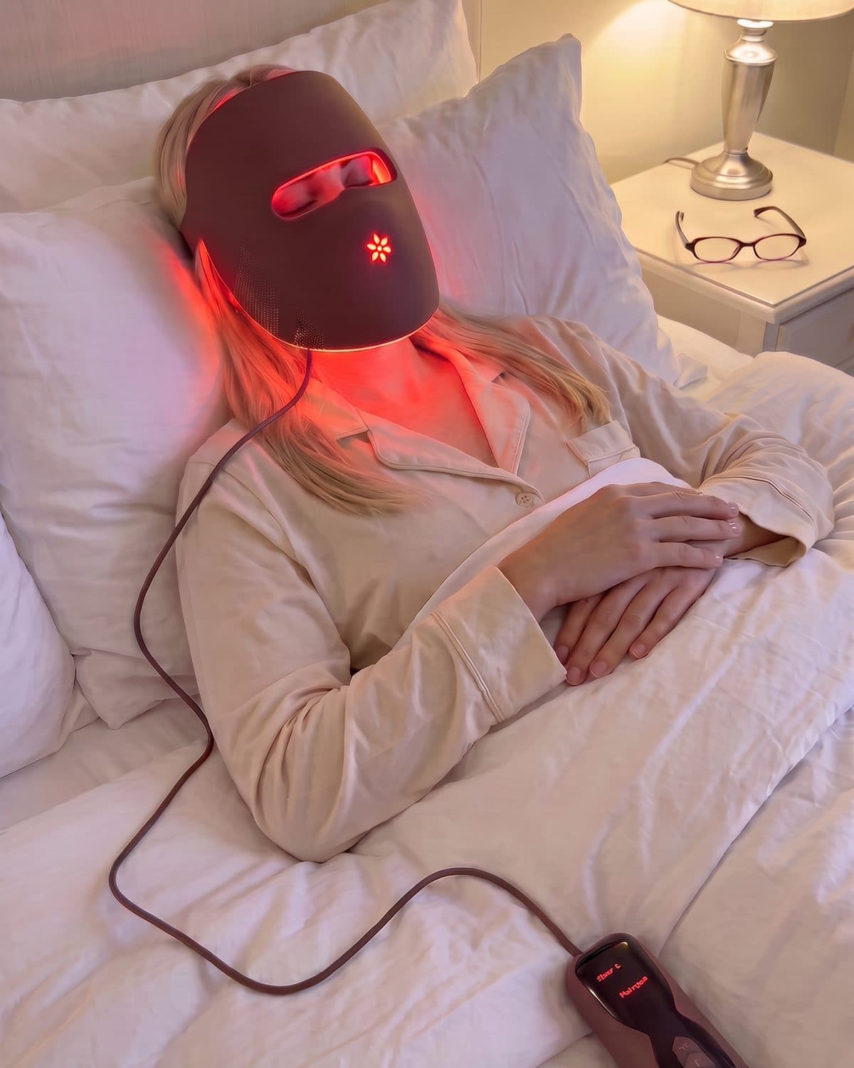 Woman lying back with the Albelys mask on and the controller resting on the duvet beside her