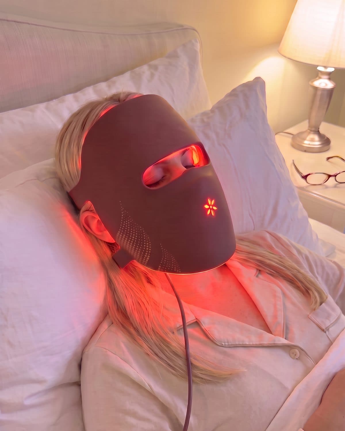 Woman lying on a pillow wearing the Albelys mask switched on, seen from above, red light on her skin