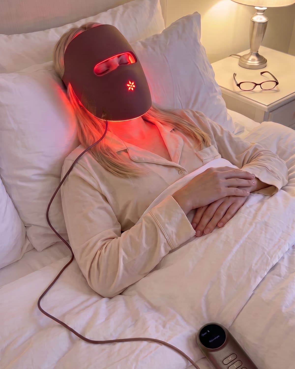 Woman lying back with the Albelys mask on and the controller resting on the duvet beside her